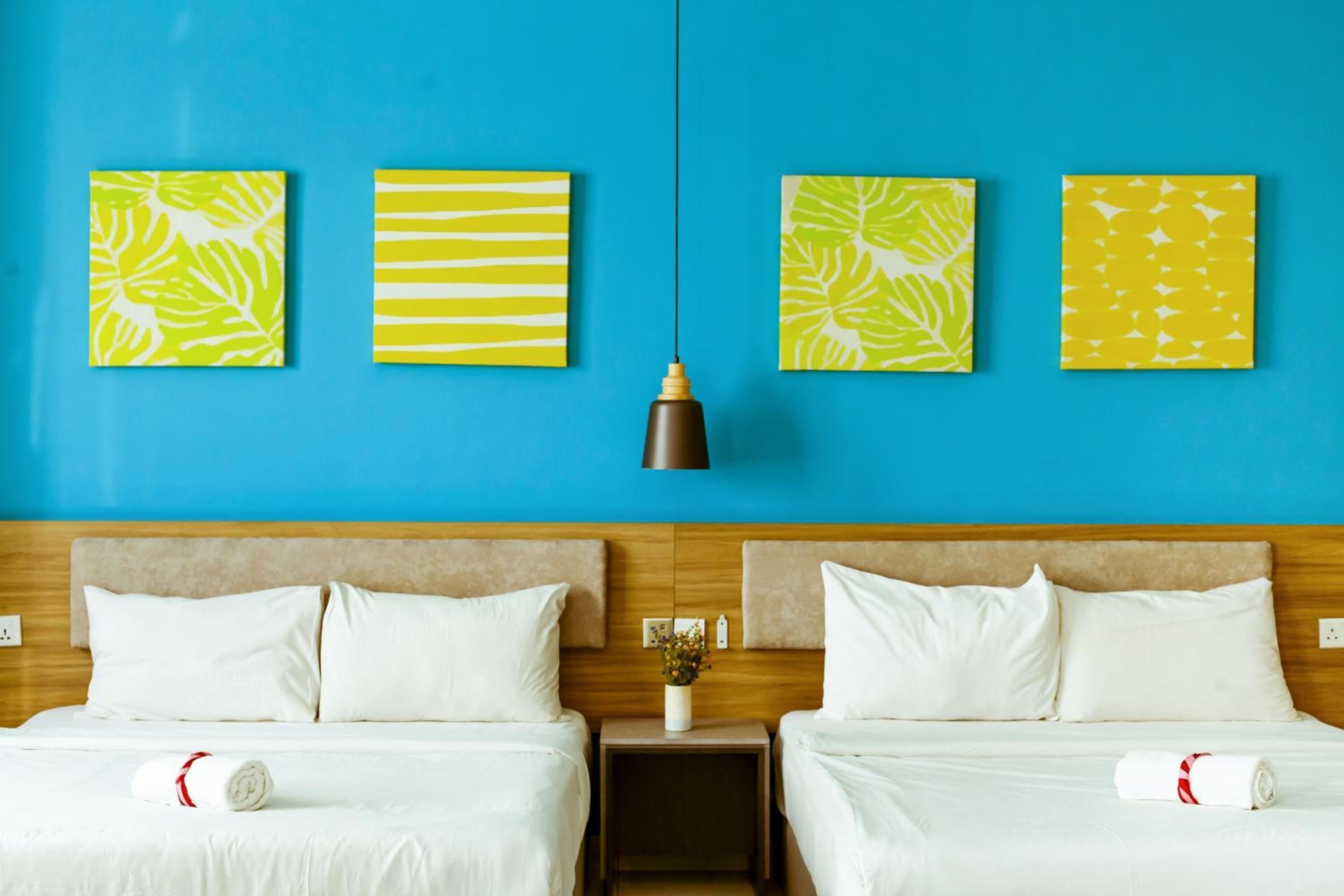 A hotel room with two beds, a blue wall, and three artwork pieces.