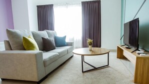 Un salon moderne avec un canapé gris, une table basse ronde, un téléviseur posé sur un meuble en bois et une fenêtre avec des rideaux.