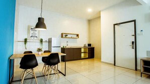 Une cuisine moderne avec un coin repas, comprenant une table en bois, des chaises noires, un luminaire suspendu et un réfrigérateur blanc.
