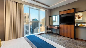 A hotel room with a large bed, a desk, a TV, and a view of the city. - Elian Hotel (Riyadh)