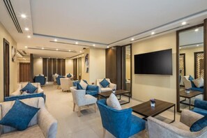A modern hotel lobby with seating areas, a large flat-screen TV, and a decorative wall panel. - Elian Alsahafa Hotel (Riyadh)