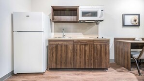 A compact kitchen with a white refrigerator, wooden cabinets, a microwave, and a sink. - Woodspring Suites Orlando Kissimmee Maingate (Kissimmee)