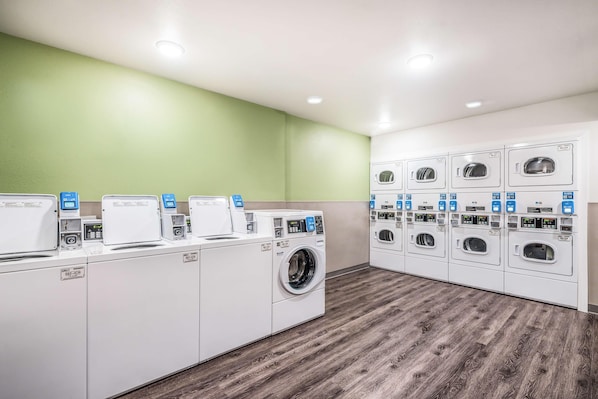 A laundry facility with multiple washing machines and dryers, a green wall, and a wooden floor. - Woodspring Suites Orlando Kissimmee Maingate (Kissimmee)