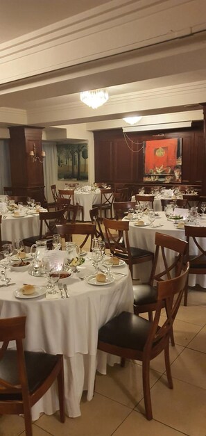 A dining area with round tables set for multiple guests, each with white tablecloths and wooden chairs. - Lingos Hotel (Florina)
