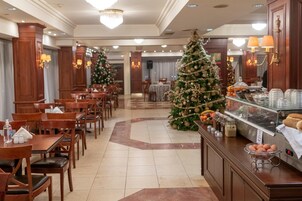 Un comedor de hotel con mesas y sillas de madera, un árbol de Navidad y un mostrador de buffet con comida.