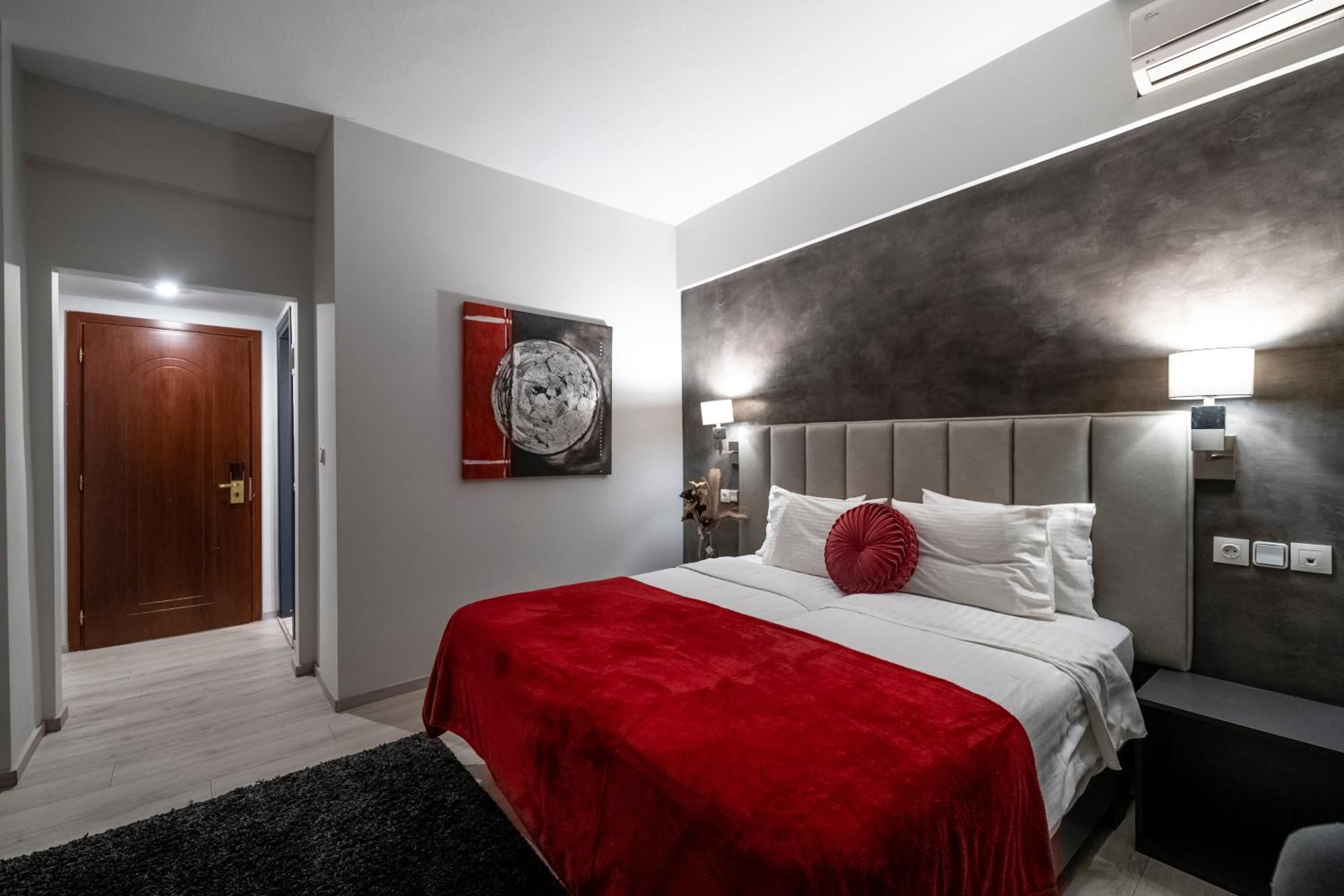 A modern bedroom with a large bed, a red throw blanket, a grey headboard, and a wall-mounted artwork.