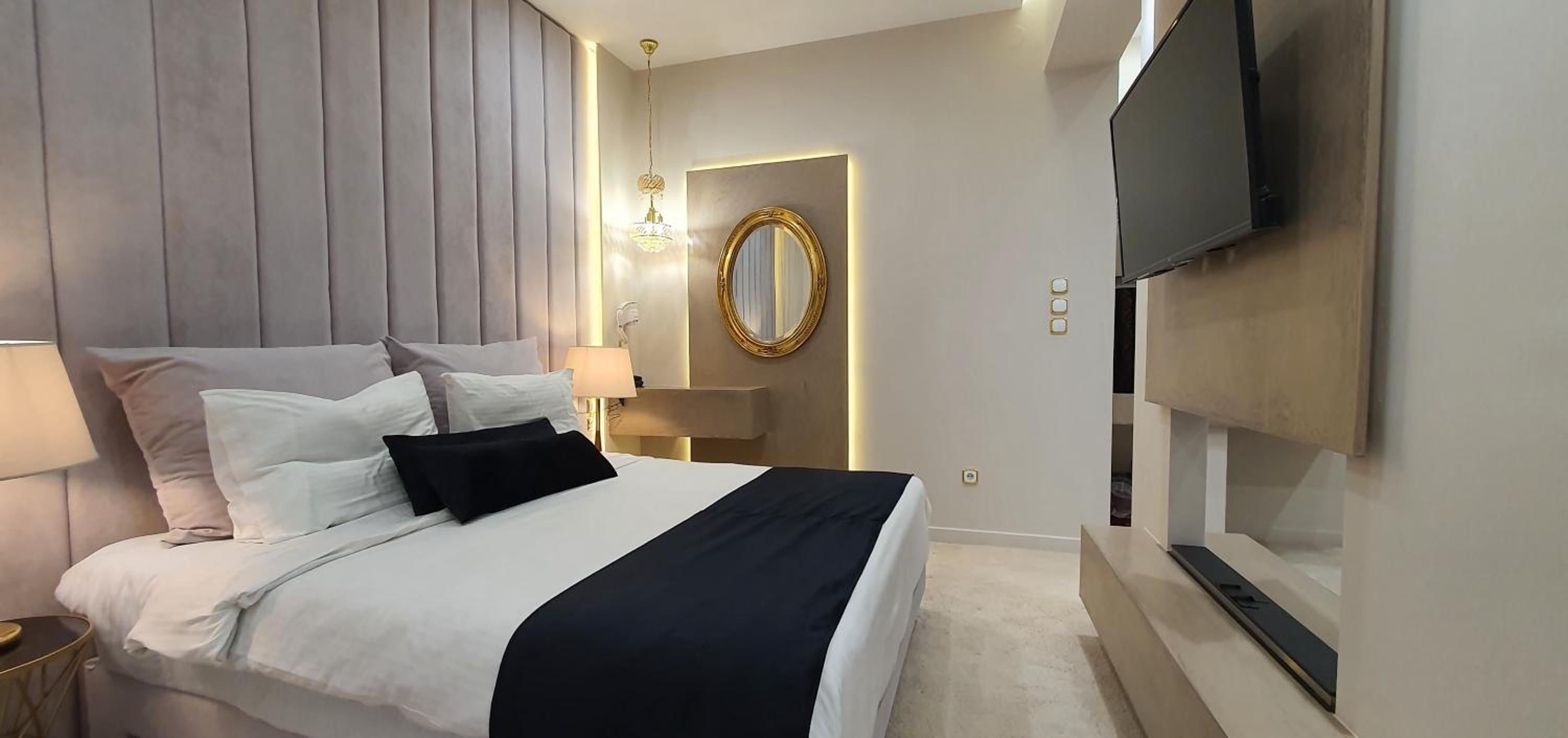 Et moderne hotelværelse med seng, sengeborde, lamper, et fjernsyn og et spejl.