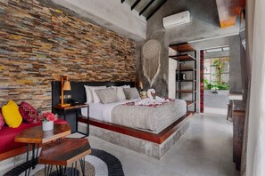 Un dormitorio moderno con una cama flotante, una pared de piedra, un atrapasueños y vistas a la vegetación exterior.