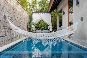 A pool area with a hammock, stone wall, and a covered seating area with plants. - Vinna Villa Seminyak (Kerobokan)