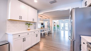A modern kitchen with white cabinets, a stainless steel refrigerator, and a wooden floor. - Ultimate Tiki Retreat - 10 Min to Beach! (Bradenton)