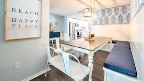 A dining area with a wooden table, white chairs, and a bench with cushions. - Ultimate Tiki Retreat - 10 Min to Beach! (Bradenton)