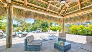 A covered outdoor lounge area with wicker furniture, a ceiling fan, and a pool in the background. - Ultimate Tiki Retreat - 10 Min to Beach! (Bradenton)