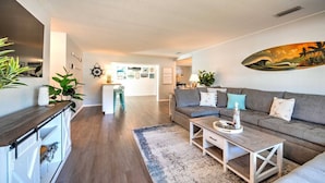 A modern living room with a grey sofa, a coffee table, and a kitchen area with a white countertop and bar stools. - Ultimate Tiki Retreat - 10 Min to Beach! (Bradenton)