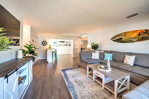 Ein modernes Wohnzimmer mit grauem Sofa, Couchtisch und Küchenbereich mit weißer Arbeitsplatte und Barhocker.