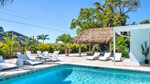 A swimming pool with lounge chairs, a thatched-roof structure, and tropical vegetation. - Ultimate Tiki Retreat - 10 Min to Beach! (Bradenton)