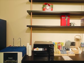 Un coin cuisine équipé d’un four à micro-ondes, de tasses empilées et d’une machine à café.