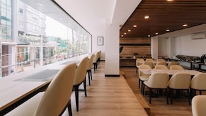 A modern hotel dining area with long tables and chairs, a wooden ceiling, and large windows offering a view of the street. - Chotel Ben Thanh (Ho Chi Minh City)