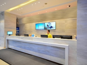 A modern reception desk with a flat-screen TV, a computer, and a mobile device. - City Comfort Inn (Wuhan)