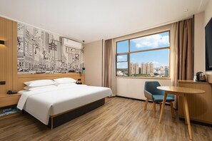 A hotel room with a large bed, a desk, a chair, a window with a city view, and a wall with a cityscape mural. - City Comfort Inn (Wuhan)