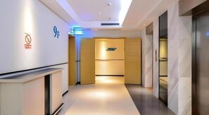 Ein Hotelgang mit einer Rezeption, einem Schild für die 9. Etage und einer Tür zu einem Zimmer.
