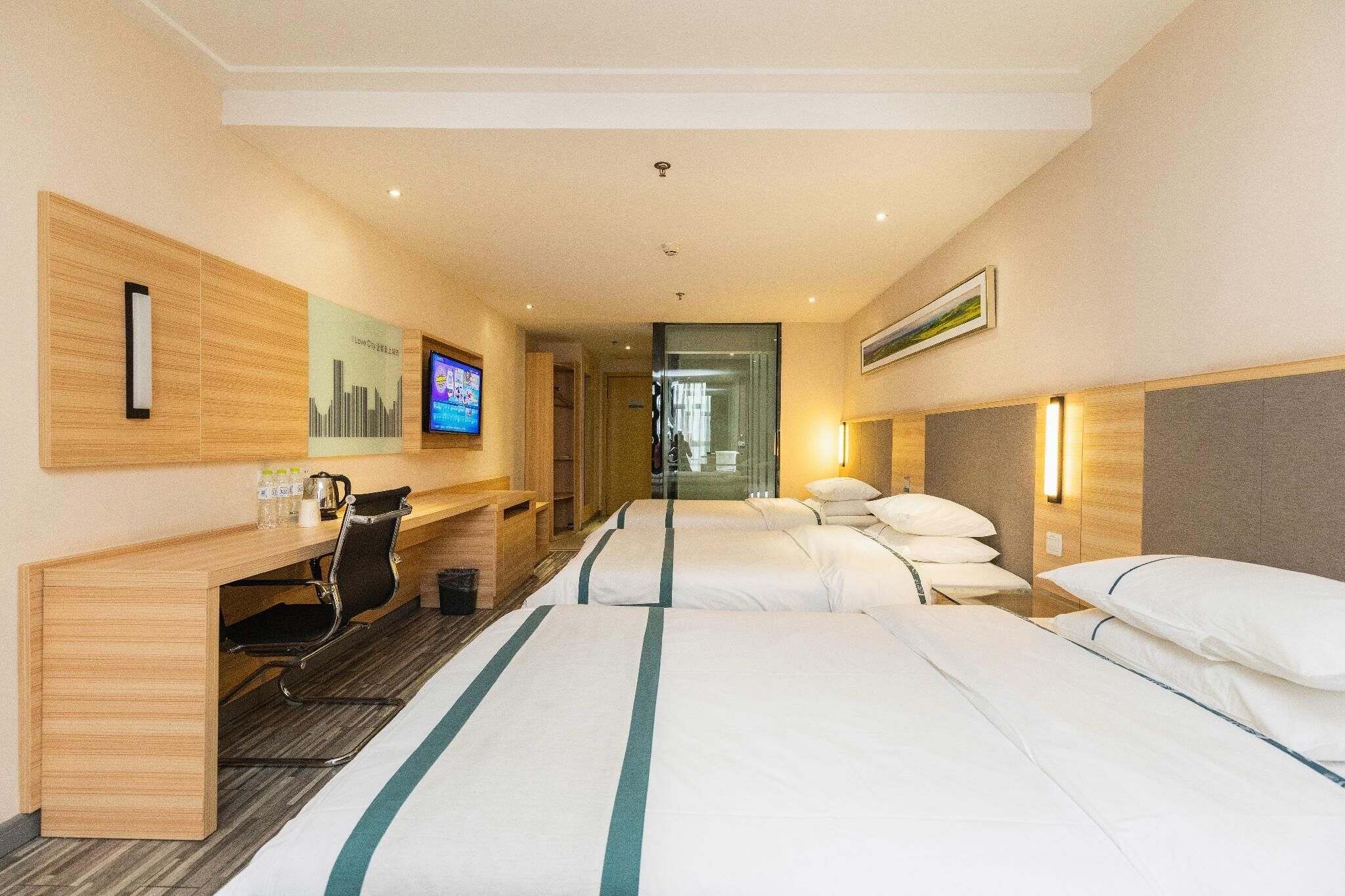 A hotel room with two beds, a desk, a chair, a television, and a bathroom visible through a glass door.