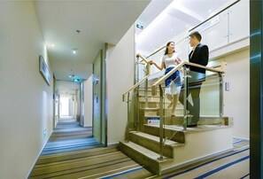 A hotel corridor with a staircase, a sign indicating a direction, and a person descending the stairs. - City Comfort Inn (Chongqing)