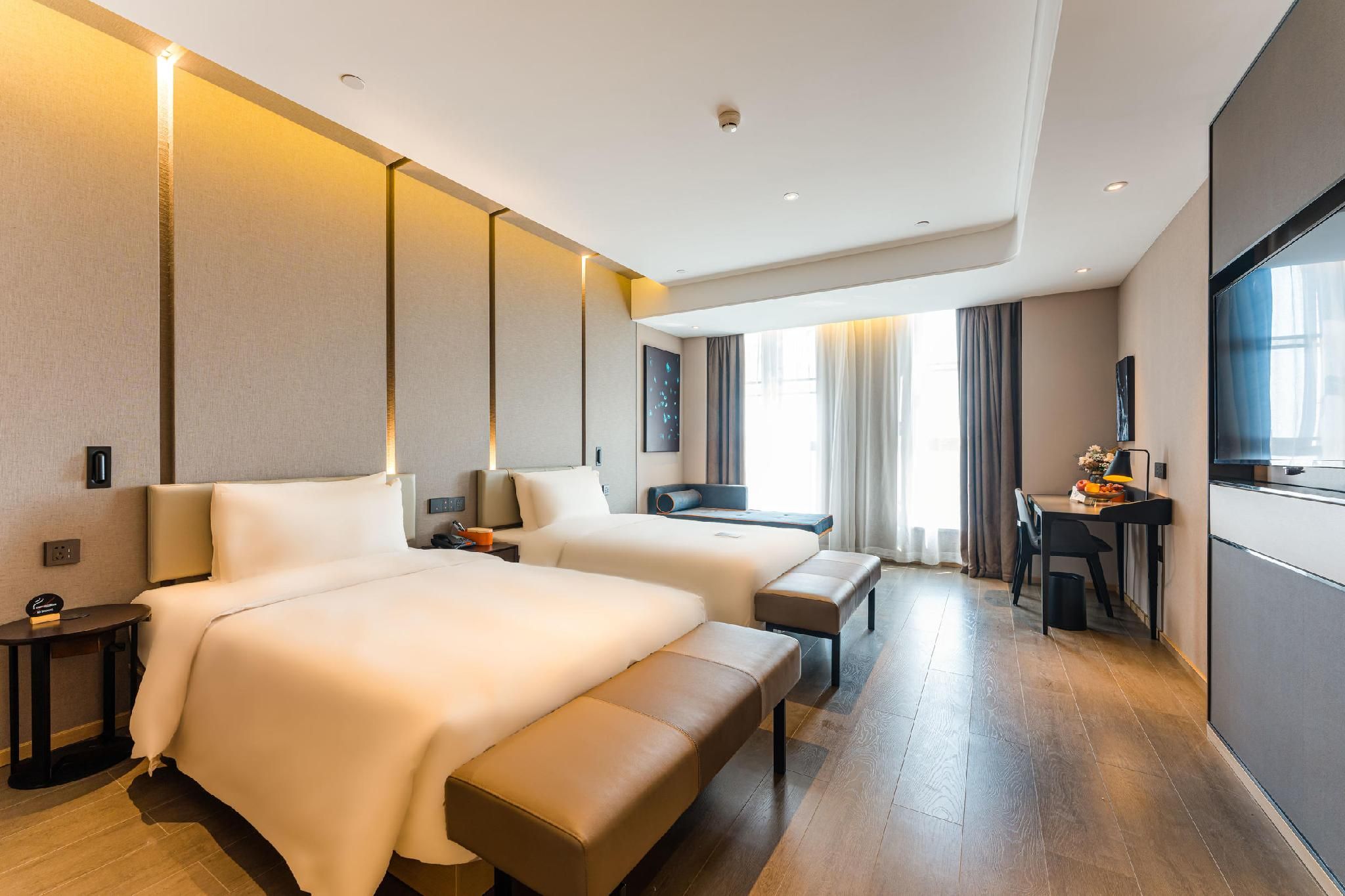 A hotel room with two beds, a desk, and a bench.