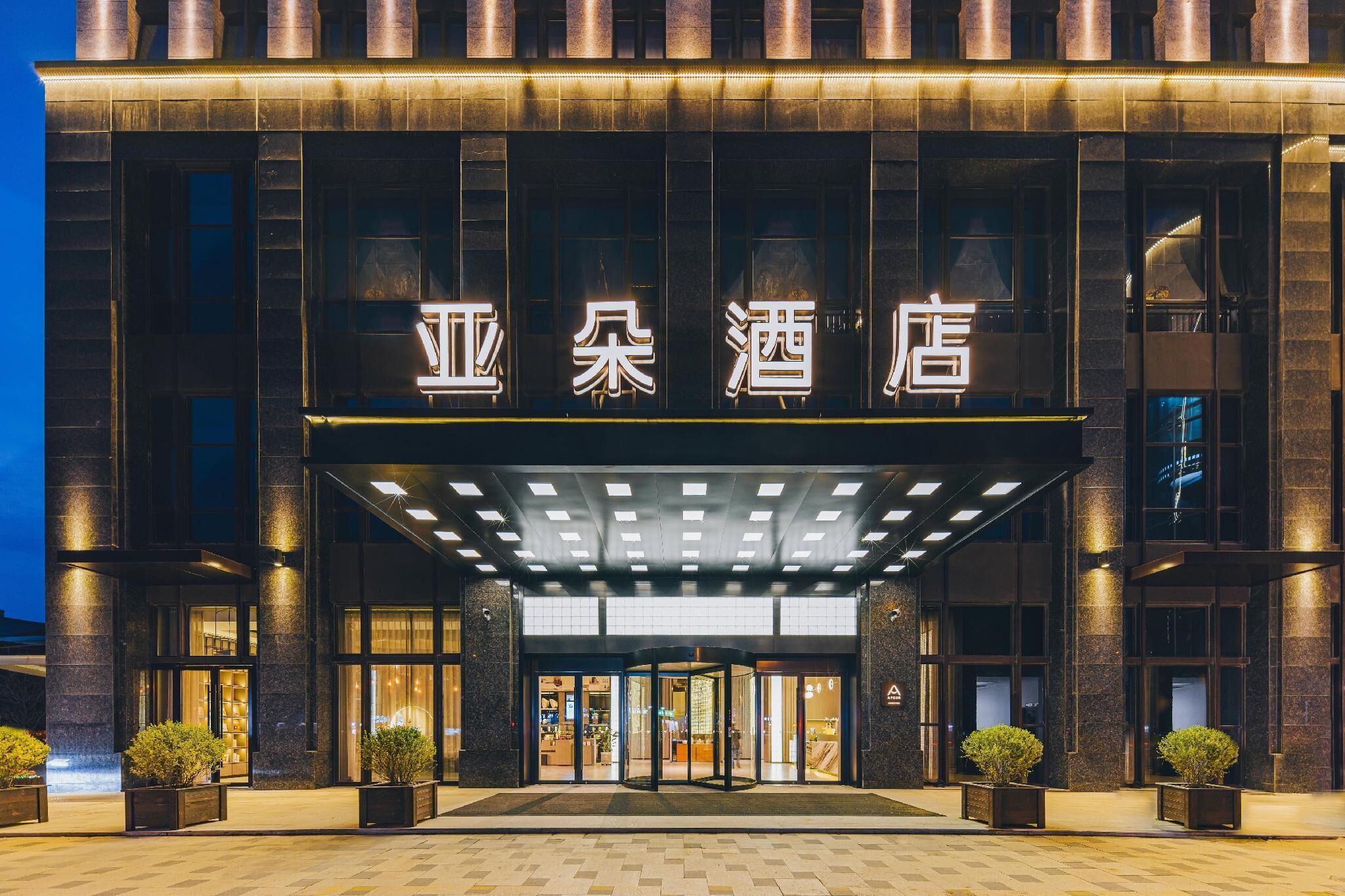 A hotel entrance with a modern design, featuring a prominent sign with Chinese characters, large glass doors, and a well-lit entrance area.