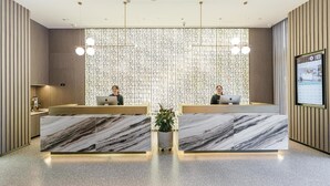 A modern reception desk with two staff members, a decorative wall, and a digital display. - Atour Hotel Haifeng Road Haiyan Jiaxing (Jiaxing)