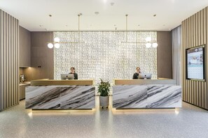 Un mostrador de recepción moderno con dos empleados, una pared decorativa y una pantalla digital.