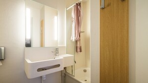 A bathroom with a white sink, a mirror, a shower curtain, and a wooden door. - B&B Hotel Saint-brieuc (Tregueux)