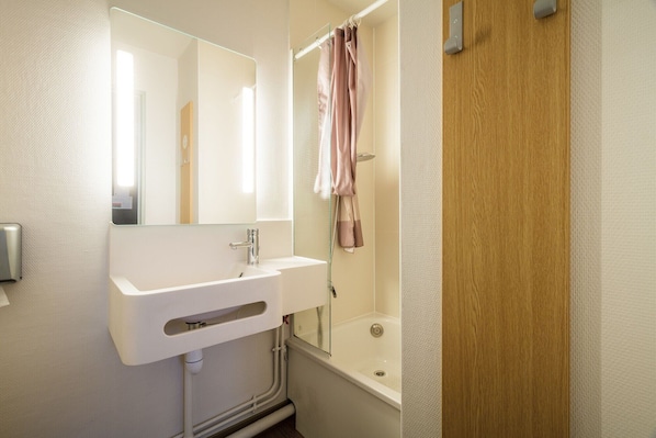 Une salle de bain avec un lavabo blanc, un miroir, un rideau de douche et une porte en bois.