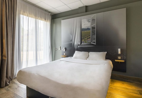 Une chambre d’hôtel moderne avec un grand lit, une vue sur un vignoble par la fenêtre et une tête de lit de couleur sombre.