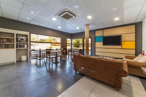 Amplia sala de estar con un sofá grande, mesa de comedor y sillas. Hay un televisor montado en la pared y una zona de cocina con electrodomésticos.
