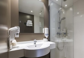 Un baño moderno con un lavamanos blanco, un espejo, un perchero para toallas y una zona de ducha con mampara de vidrio.