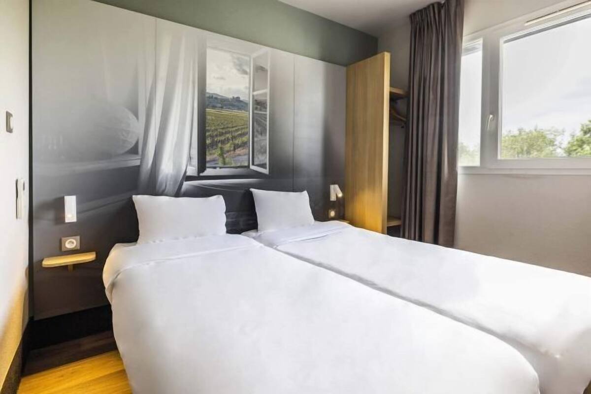 Una cama doble con ropa blanca, una mesita de noche, una lámpara y una ventana con vistas al paisaje.