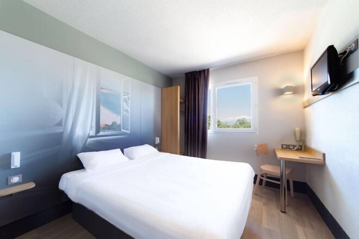Una habitación de hotel con cama, escritorio, silla, televisor y ventana.