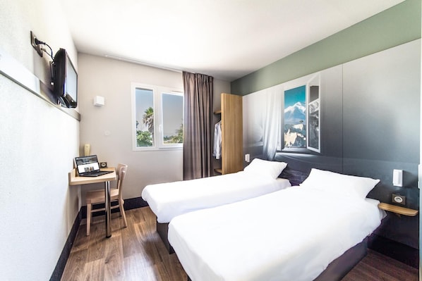 Habitación de hotel con dos camas, un escritorio con una computadora portátil, una silla, una ventana con cortinas y un cuadro en la pared.