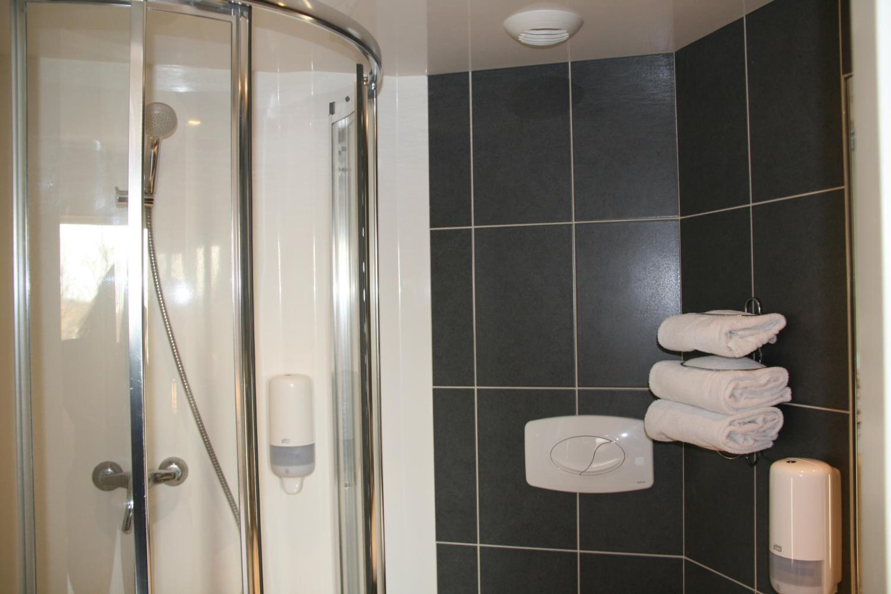 A shower with a glass door, a hand dryer, and a towel rack with folded towels.