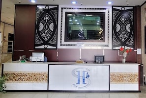 A reception desk with a large logo, a computer, and a small plant. - SHH Hotel (Al-Fujairah)