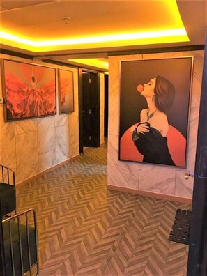 A hallway with marble walls and a herringbone floor. There are two large framed artworks on the walls. - SHH Hotel (Al-Fujairah)