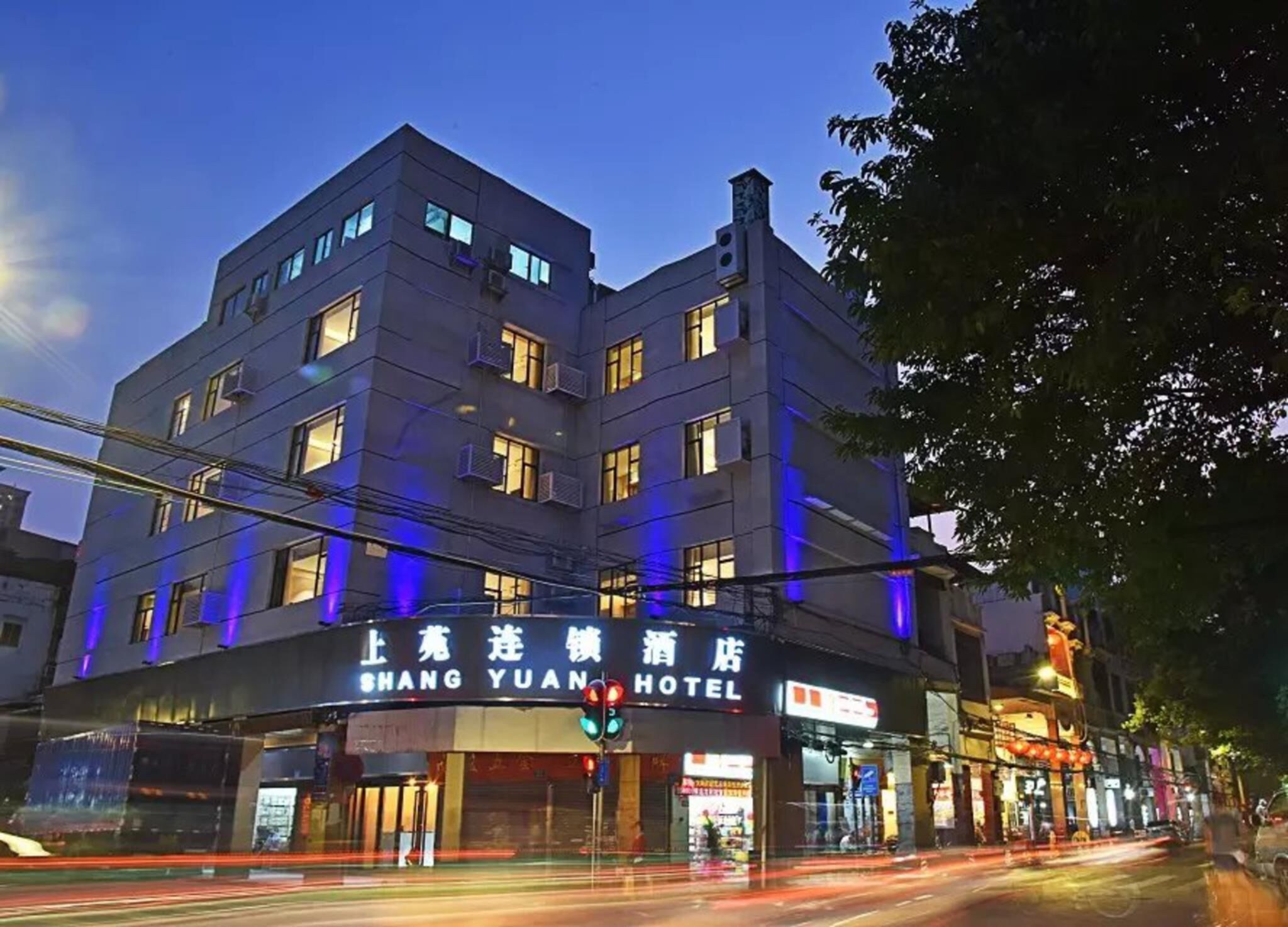 Un hotel de varios pisos con señalización iluminada, una entrada visible y vista a la calle con semáforos.