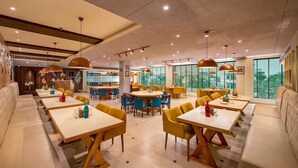A modern dining area with multiple tables and chairs, a bar area, and large windows offering a view.