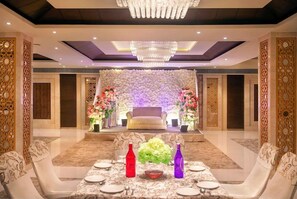 A banquet hall with a floral backdrop, a stage, and a chandelier. - Bloom Boutique Ranjit Avenue (Amritsar)