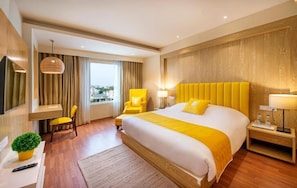 Habitación de hotel con una cama grande, un escritorio, una silla, un televisor y vistas a la ciudad.