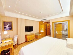 Une chambre d’hôtel comprenant un lit, une télévision, un bureau avec une lampe, une chaise, une commode et une armoire.