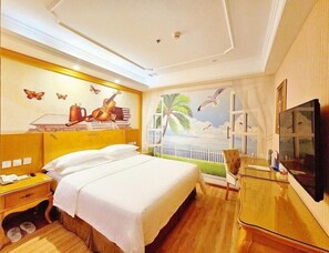 Ein Hotelzimmer mit Bett, Nachttisch, Schreibtisch mit Stuhl, Fernseher und Wandgemälde mit Strandmotiv.