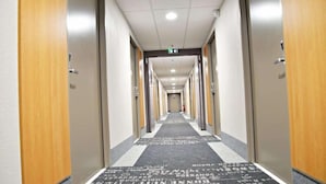 A hotel hallway with a carpet featuring foreign text, wooden doors, and a ceiling with recessed lighting. - B&B Hotel Ales Pole Mecanique (Saint-Martin-de-Valgalgues)