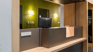 A reception desk with a computer, two wall-mounted lamps, and a wooden counter. - B&B Hotel Ales Pole Mecanique (Saint-Martin-de-Valgalgues)