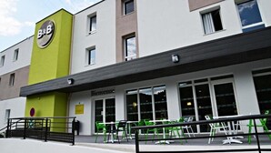 A B&B hotel with a green and white facade, a 'Bienvenue' sign, and outdoor seating with green chairs. - B&B Hotel Ales Pole Mecanique (Saint-Martin-de-Valgalgues)